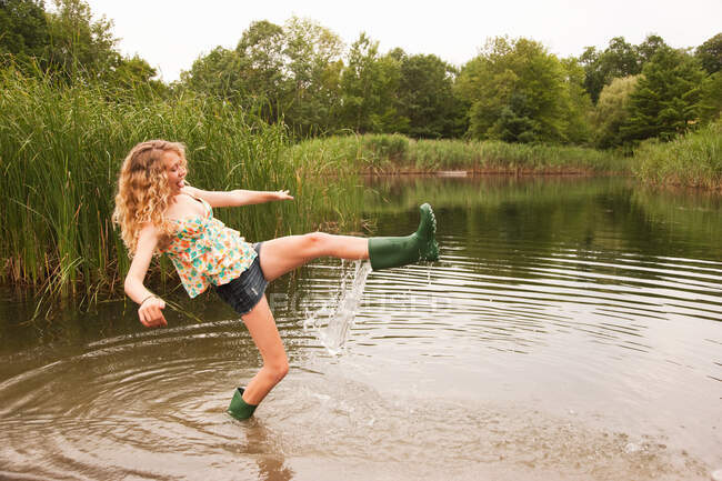 Teenage girl wading into the middle of a lake with over-flowing wellies — Stock Photo