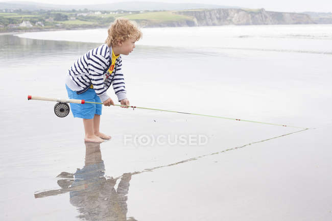 Menino de pé na praia com vara de pesca — Fotografia de Stock