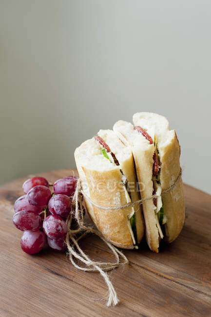 Chiabata sandwiches and grapes on wooden table — Stock Photo