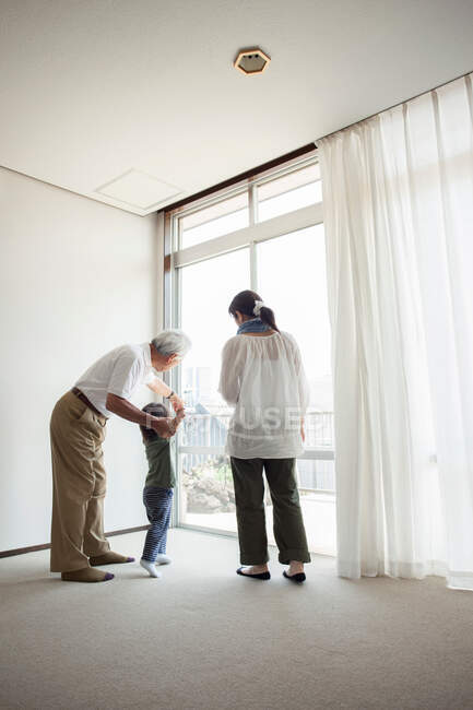 Familia de tres generaciones de pie junto a la ventana - foto de stock