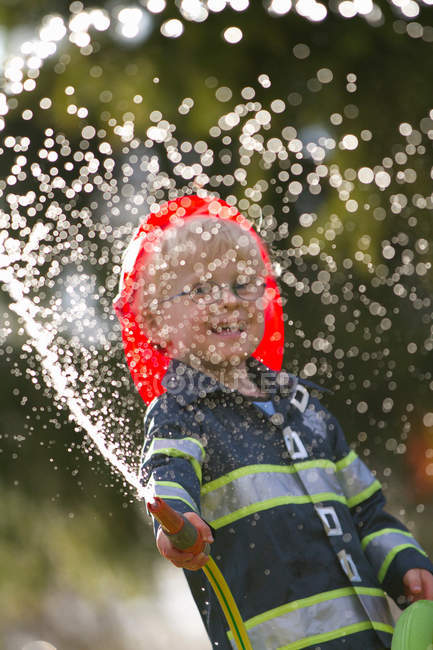 Menino em traje de bombeiro brincando com mangueira — Fotografia de Stock
