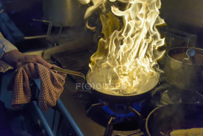 Chef with pan of flames in traditional Italian restaurant kitchen, close up — Stock Photo