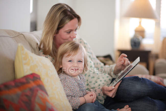 Mãe e filha no sofá com tablet digital — Fotografia de Stock