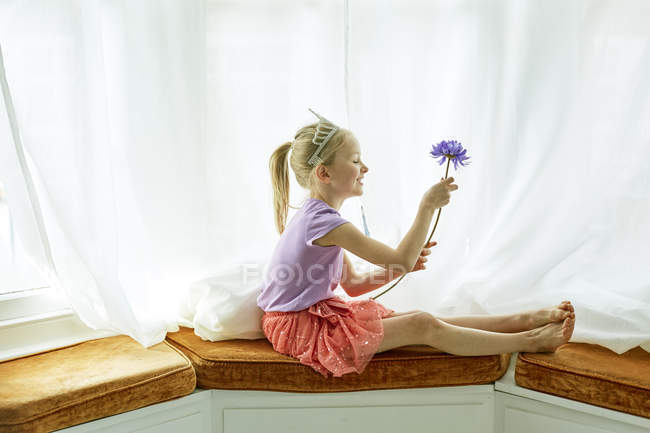 Girl wearing tiara, holding flower at bay window — Stock Photo