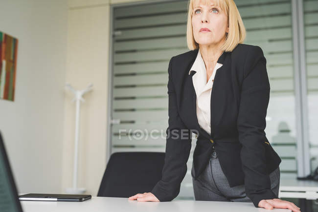 Mujer de negocios madura seria inclinándose hacia adelante en el escritorio de la oficina - foto de stock