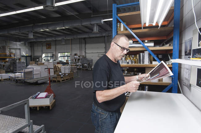 Працівник перевіряє якість поліграфічної продукції в поліграфічній майстерні — стокове фото