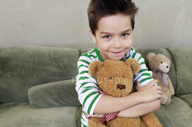Portrait of young boy on sofa hugging teddy — Stock Photo