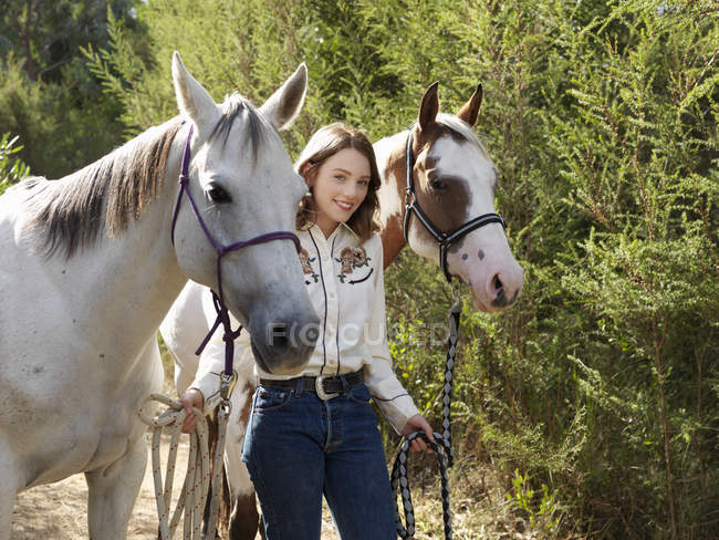 Portrait of teenage girl leading two horses — Stock Photo