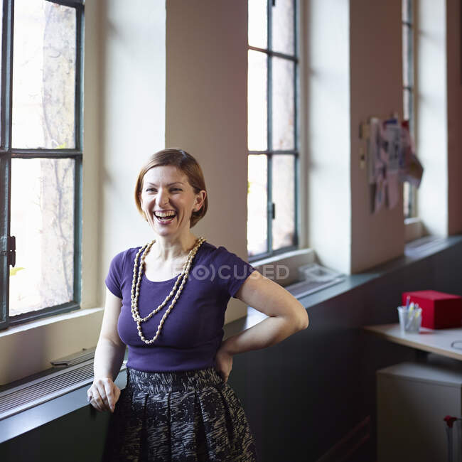 Mitte erwachsene Frau am Fenster, lachend — Stockfoto