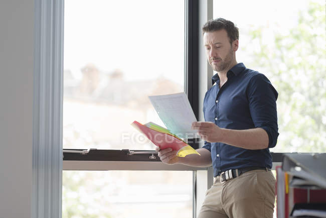 Homem contemplando e lendo papéis pela janela do escritório — Fotografia de Stock