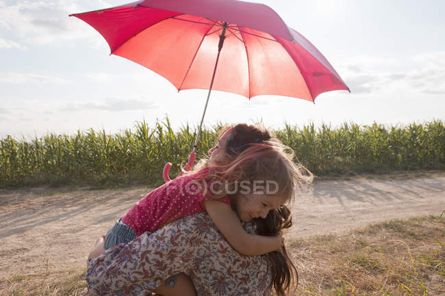 Мать и дочь обнимаются под красным зонтиком — стоковое фото