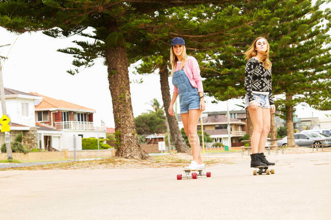 Two young women skateboarding through tree lined street — Stock Photo