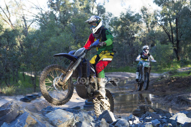 Dos jinetes de motocross macho jóvenes corriendo a través del río bosque - foto de stock