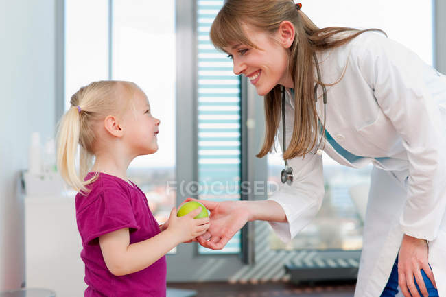 Doctor handing girl an apple in office — Stock Photo
