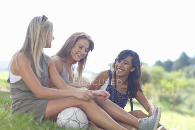 Троє друзів сидять на траві спілкуючись — стокове фото