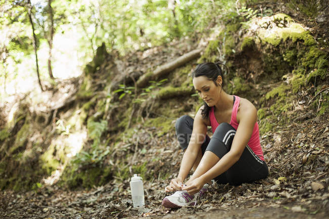 Female jogger tying shoelace in forest — Stock Photo