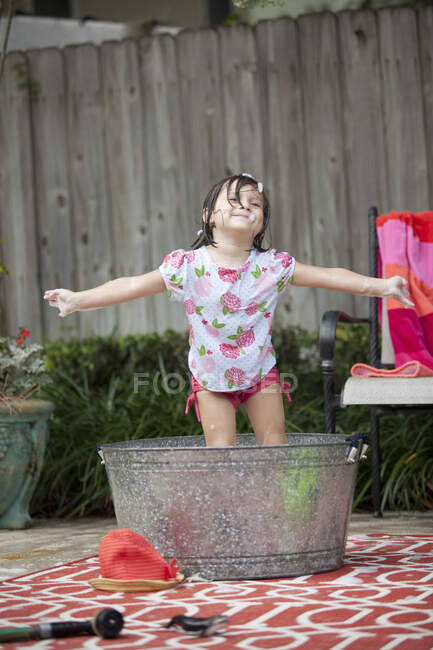Mädchen steht mit ausgestreckten Armen in Badewanne im Garten — Stockfoto