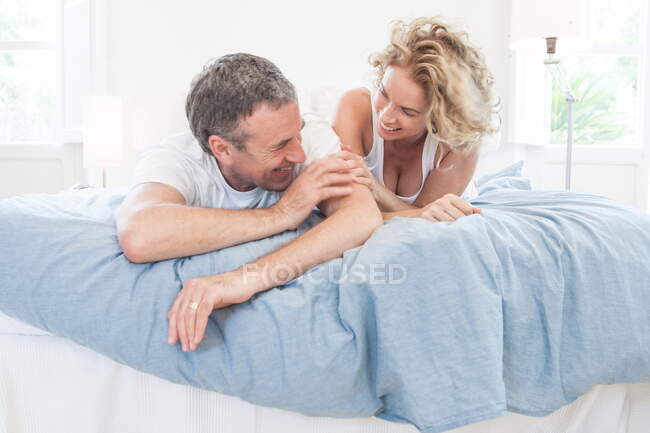 Reifes Paar liegt lachend auf Bett — Stockfoto
