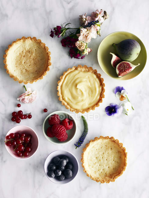 Пустые и наполненные пироги с фруктами и цветами на столе — стоковое фото