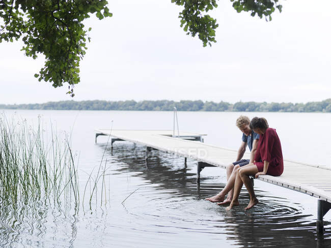 Paar sitzt nebeneinander auf einem Steg und taucht Zehen in Wasser, Kopenhagen, Dänemark — Stockfoto