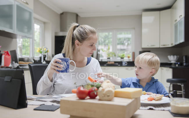 Madre e hijo sentados a la mesa comiendo juntos - foto de stock