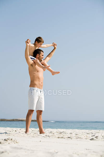 Отец несет сына на плечах на пляже — стоковое фото
