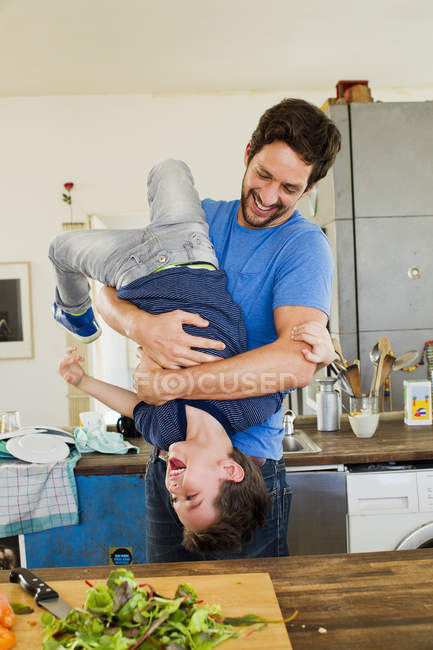 Father holding little son upside down in kitchen — Stock Photo