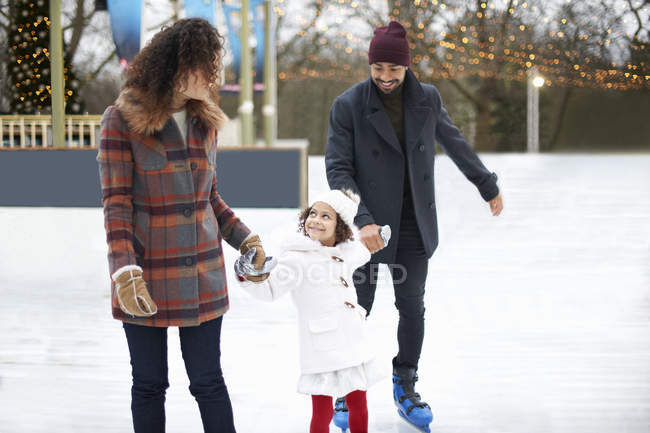Девушки катаются на коньках, держатся за руки с родителями, смотрят вверх улыбаясь — стоковое фото