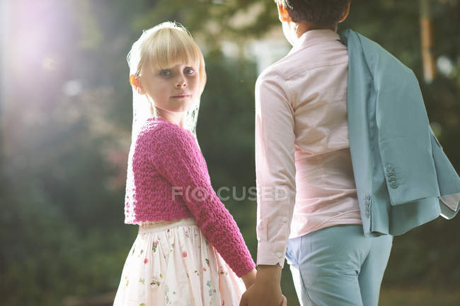 Mädchen blickt über ihre Schulter, während es Jungen die Hand im Garten hält — Stockfoto