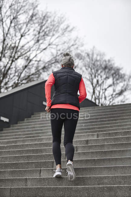Вид ззаду зрілої жінки бігунка біжить по міських сходах — стокове фото