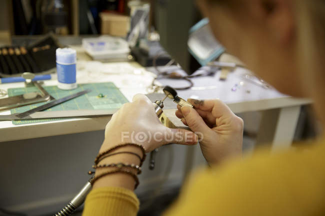 Over shoulder view of female jewellery maker using miniature drill in design studio — Stock Photo