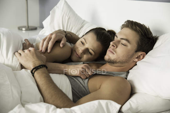 Молода пара лежить в ліжку обіймає — стокове фото
