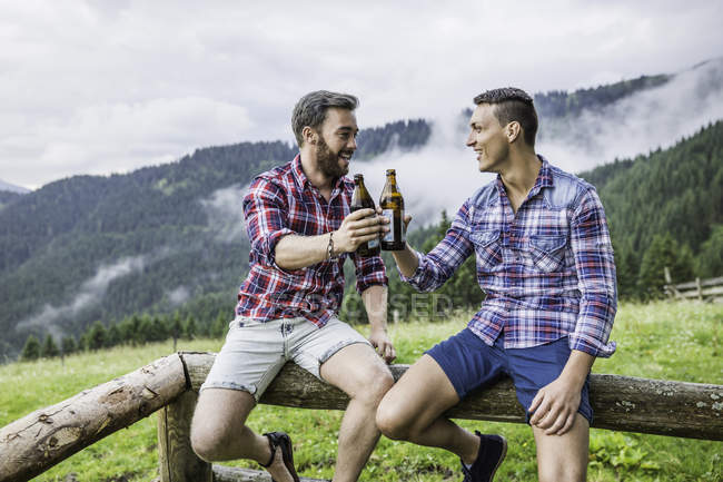 Two male friends drinking beer on fence — Stock Photo
