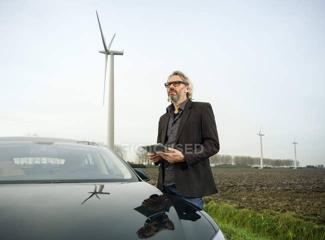 Людина на машині з вітровою турбіною на задньому плані — стокове фото