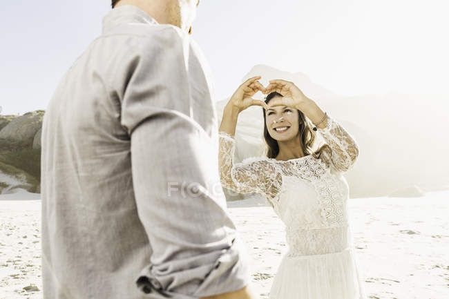 Woman making heart shape with hands for boyfriend on sunlit beach, Cape Town, South Africa — Stock Photo