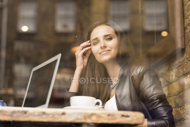 Window view portrait of young businesswoman with laptop in cafe — Stock Photo