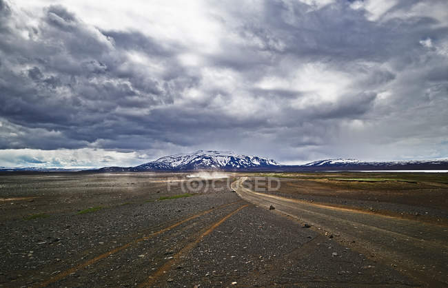 Pista sterrata in un paesaggio arido con drammatico cielo nuvoloso — Foto stock