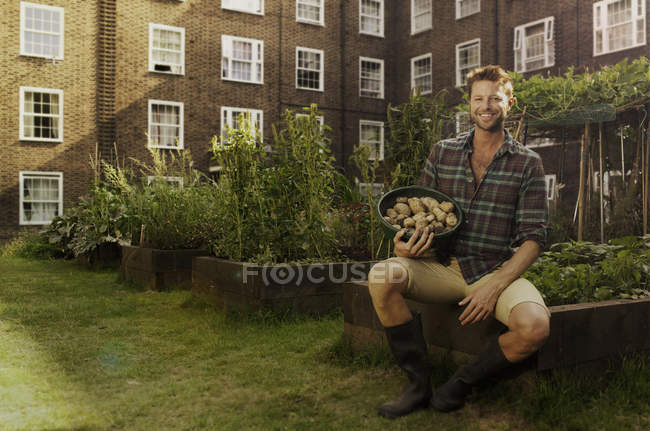 Man on council estate allotment with bowl of potatoes — Stock Photo
