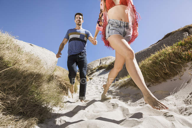 Couple outdoors, holding hands, running down towards beach, low angle view — Stock Photo