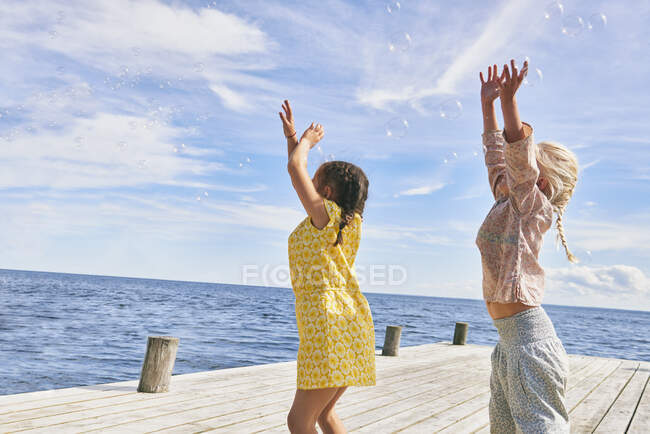 Due giovani amici che giocano sul molo di legno, raggiungendo le bolle — Foto stock
