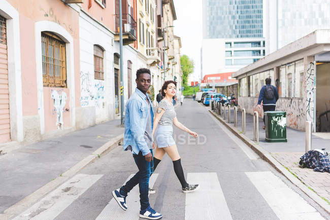 Pareja caminando a través del cruce peatonal, Milán, Italia - foto de stock