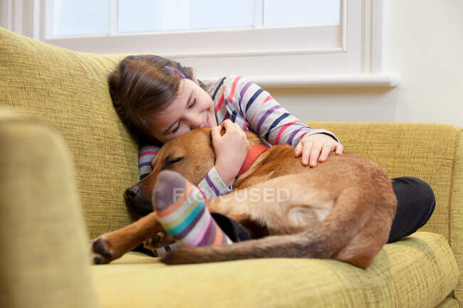 Jovem menina abraçando seu cão no sofá — Fotografia de Stock