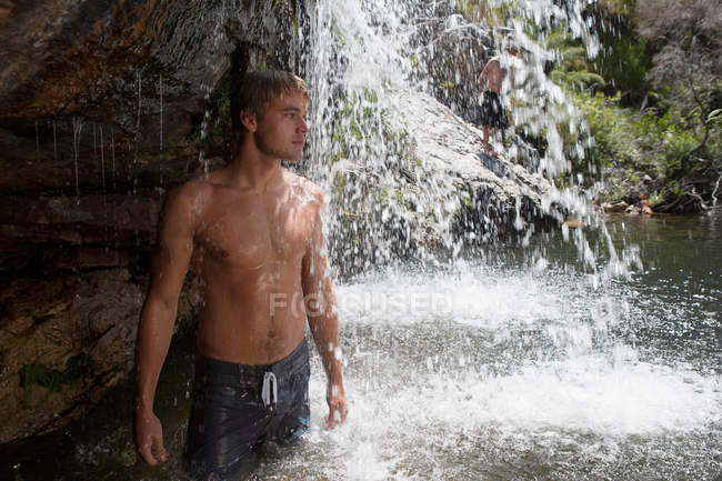 Молодий чоловік стоїть під водоспадом, дивлячись — стокове фото