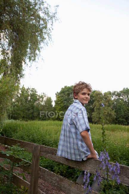 Kleiner Junge sitzt auf Zaun und schaut in die Kamera — Stockfoto