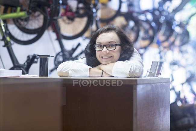 Frau am Schalter in Fahrradgeschäft blickt lächelnd in Kamera — Stockfoto