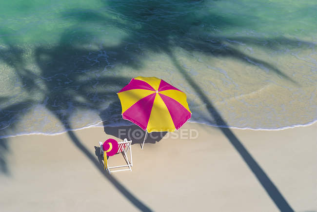 Deckchair and parasol on seashore with palm shadows — Stock Photo