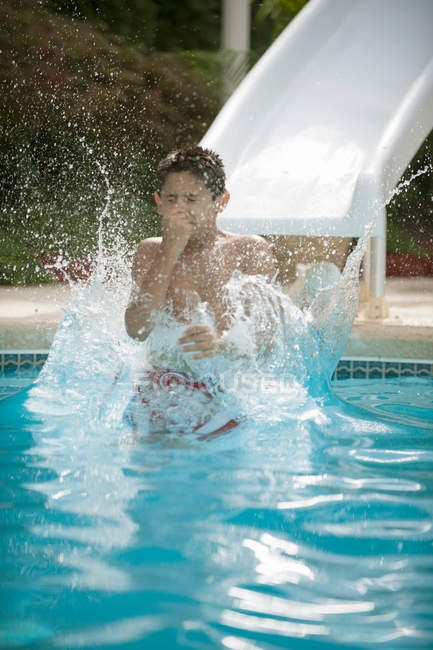 Junge planscht auf Wasserrutsche in Pool — Stockfoto