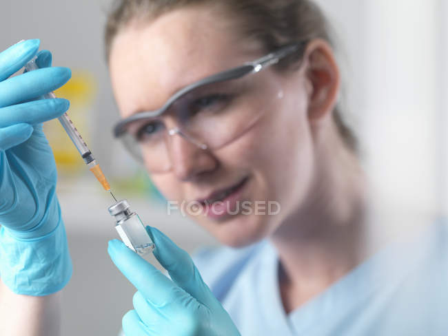 Медицинский работник держит в руках шприц и флакон, наполняя шприц при инъекции препарата — стоковое фото