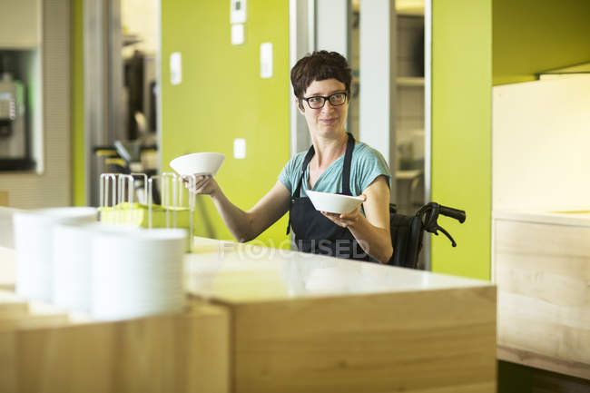 Femme en fauteuil roulant, travaillant dans un restaurant, tenant des bols — Photo de stock