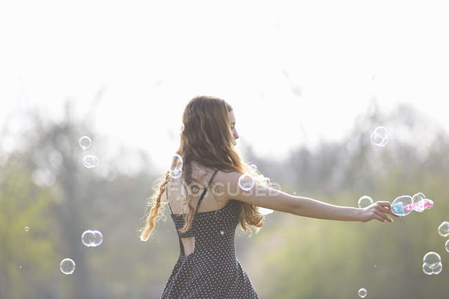 Дівчина-підліток обертається бульбашками з бульбашковою паличкою в парку — стокове фото